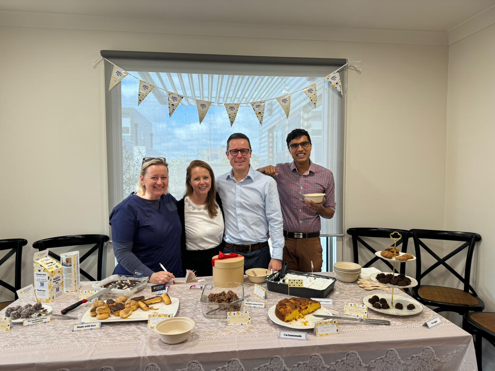 Doctors smile at the camera in front of a table laden with baked goods