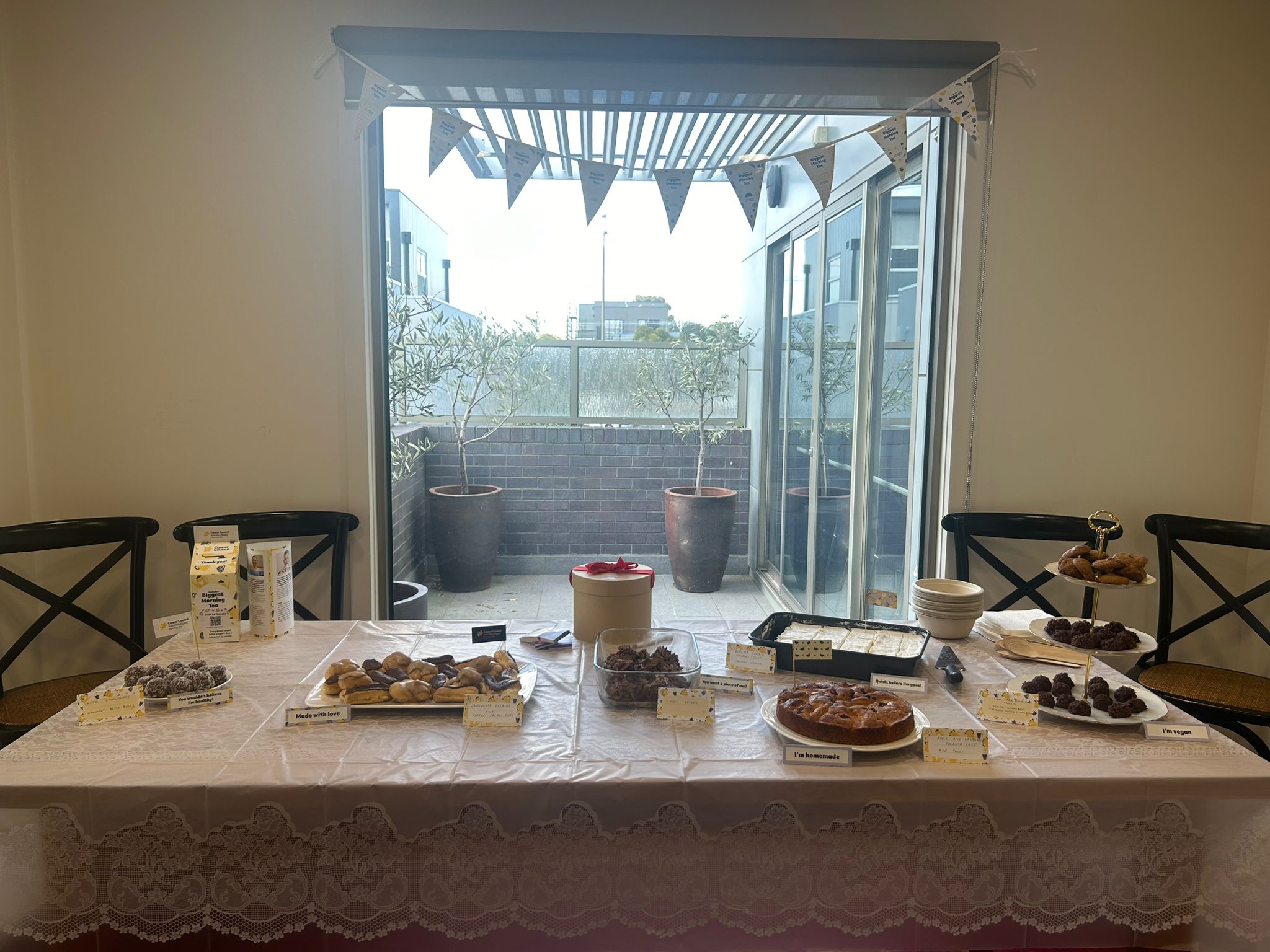 Table filled with different baked goods in front of a window with bunting