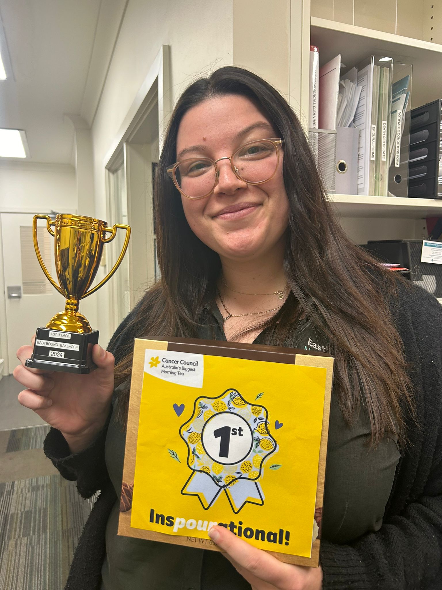 Woman smiles at camera while holding a first place placard and a small gold trophy